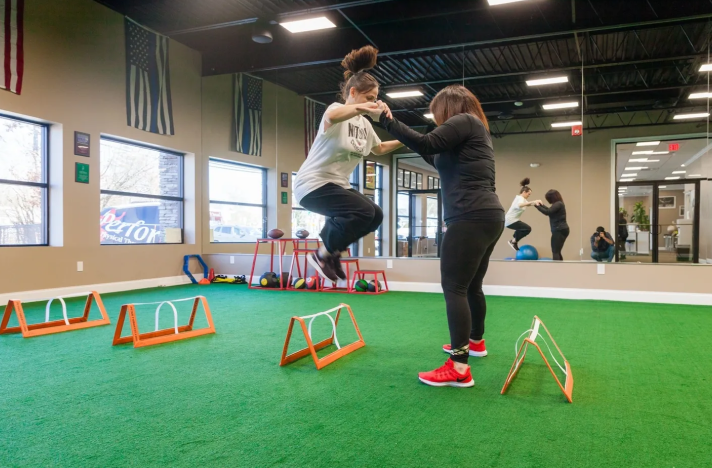 Two women are practicing their jumps in a gym.